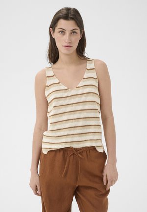 Jeune femme aux longs cheveux bruns portant un débardeur tricoté sans manches crème et marron rayé et un pantalon marron ample à cordon.