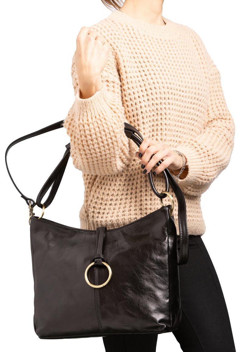Borsa a mano in pelle nera con una texture liscia, caratterizzata da un accento circolare dorato e una zip superiore, indossata su una tracolla.