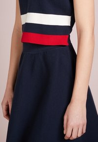 Stickad klänning i marinblått med röda och vita ränder vid midjan. Utsvängd kjoldesign med texturerat tyg och figurnära bodice.