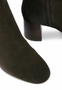 Ciemnozielone zamszowe botki za kostkę z ostrym noskiem, subtelnym przeszyciem i drewnianym obcasem typu słupek. Z boku zamek błyskawiczny dla łatwego zakładania.