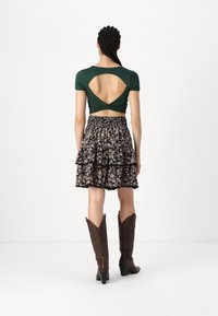 Green short-sleeve top with back cutout, paired with a black floral tiered skirt and brown cowboy boots featuring pointed toes and heels.