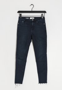 Jeans skinny de color azul oscuro con dobladillo deshilachado, hechos de mezclilla, que cuentan con bolsillos delanteros y una cremallera con cierre de botón.