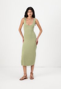 Ribbet, lang olivenfarget kjole med dyp utringning, slim fit og midt på leggen lengde. Kombinert med lysebrune sandaler med stropper.