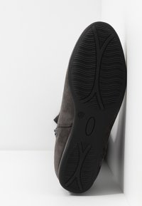 Zapato de ante gris con suela de goma texturada negra, con puntera redondeada y cierre de cremallera en el lateral. Marcado de tamaño visible en la suela.
