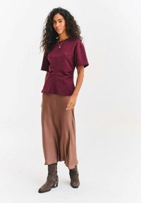 Vínový top s krátkym rukávom a bočným riasením, kombinovaný s dlhou hnedou saténovou sukňou a hnedými semišovými členkovými čižmami.