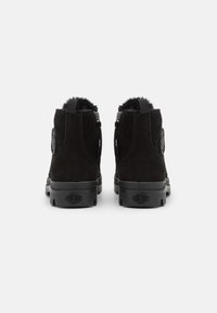 Black suede ankle boots with a soft fur lining, rounded toe, side zippers, and textured rubber soles. Features logo accents on the sides.