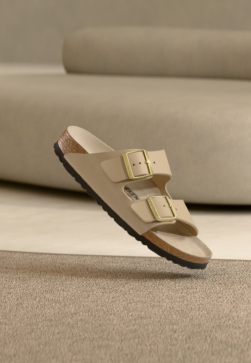 Μπεζ σανδάλι με διαφάνεια, δύο ρυθμιζόμενες χρυσές αγκράφες, μαλακό πέλμα και υφή μεσοφόρι από καφέ φελλό. Μαύρη λαστιχένια σόλα για καλύτερη πρόσφυση.