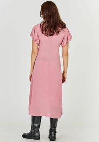 Vaaleanpunainen midimekko, jossa on liehuvat hihat ja suora leikkaus. Yhdistetty mustiin polviasusteisiin, joissa on sileä pinta ja minimaalinen yksityiskohtaisuus.