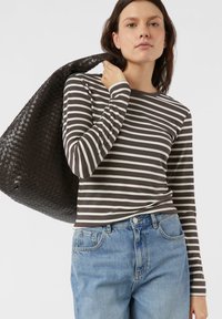 Koszula z długim rękawem w brązowo-kremowe paski, lekka tkanina, okrągły dekolt, zestawiona z niebieskimi dżinsami oraz plecioną czarną torbą.