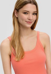 Korallenfarbenes, geripptes Tanktop mit dünnen Trägern und rundem Ausschnitt. Der Stoff hat eine glatte Textur und eine körpernahe Passform.