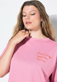 Rosa Baumwoll-T-Shirt mit kurzen Ärmeln und Rundhalsausschnitt. Mit orangefarbenem gesticktem Text: "Paris ist immer eine gute Idee, mein Freund."