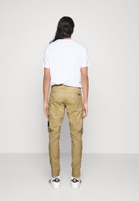 Lätta beige cargobyxor med sidofickor och svarta detaljer, tillsammans med en enkel vit T-shirt med rund halsringning och sneakers.