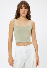 Top corto ajustado de color verde claro con escote cuadrado y tirantes anchos, hecho de material suave. Combinado con pantalones blancos de cintura alta.