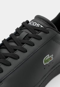 Sort læder sneakers med sorte snørebånd, med hvid logo tekst og en grøn broderet krokodille detalje på siden. Glat tekstur.
