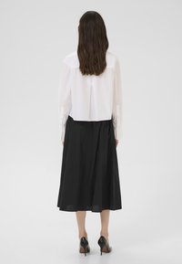 Bela skrčena majica v kombinaciji z dolgo črno krilo. Majica ima dolge rokave in ravno kroj; krilo je nagubano in zračno.