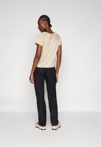 Beige short-sleeve top with a back seam detail, paired with black cargo pants featuring side pockets and a relaxed fit. Casual footwear completes the look.