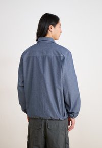 Denim jacket in medium blue with a structured collar and elastic cuffs. Features a straight cut and adjustable hem for a relaxed fit.