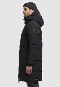 Sort pufferjakke med hætte, der har en lynlåslomme, ribbede manchetter og et elegant quiltet design.