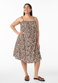 Leopardmuster-Kleid mit dünnen Trägern, gerafft im Oberteil und mit schwingendem Rock. Braune Riemchensandalen mit Nieten. Glattes Material; knielanges Design.