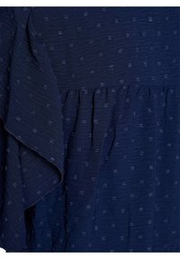 Tessuto di un blu navy strutturato con sottili punti in rilievo, caratterizzato da un bordo arricciato. Materiale morbido con un design fluido e vita arricciata.