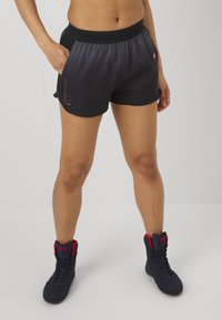 Schwarze Sportshorts mit einem Mesh-Bund und roten Akzenten, ausgestattet mit Taschen und einer glatten Textur, kombiniert mit blauen High-Top-Sneakers.