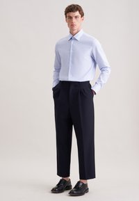 Jasnoniebieska koszula w kratę z kołnierzem typu sprawdzian, zestawiona z granatowymi, wysokim stanem spodniami i czarnymi skórzanymi butami. Zaprojektowana na miarę dopasowania.