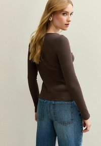 Bruin geribbeld lange mouwen top gecombineerd met blauwe high-waisted jeans. Heeft een slim fit en een ronde halslijn met subtiele textuur en naaddetails.