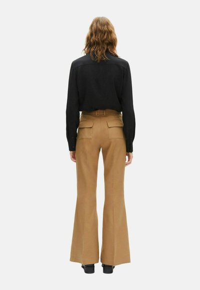 Zwarte langekiet met een gladde textuur, gecombineerd met high-waisted, flared beige broeken met twee achterzakken.
