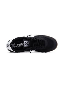Zapatillas de lona negras con acentos blancos, diseño de cordones, suela de goma y logotipo impreso en la lengua, con un perfil bajo y textura mínima.