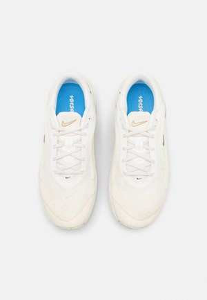 Hvide Nike løbesko med beige accenter, lyseblå indlægssåler og snørebånd, vist fra oven mod en ensfarvet hvid baggrund.