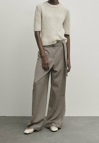 Helles beiges, geripptes Kurzarm-Pullover, kombiniert mit lockeren, tanfarbenen strukturierten Hosen und cremefarbenen Ballerinas. Glatte, weiche Materialien durchgehend.