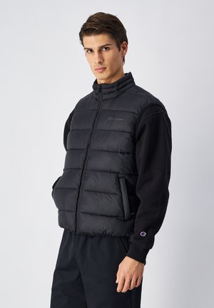 Zwarte puffer vest met hoge kraag, ritssluiting en twee zijzakken. Heeft een doorgestikt patroon en een subtiele logo op de borst.