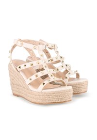 Sandalias blancas de cuña con una plataforma de yute trenzado. Presenta múltiples tiras de cuero decoradas con tachuelas doradas. Cierre de hebilla en el tobillo.