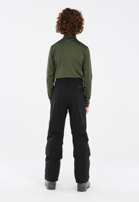 Pantaloni da neve neri e una maglietta verde a maniche lunghe sono indossati, con la vista posteriore che mostra un design aderente e linee semplici e pulite.