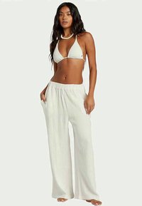 White ribbed bikini top with triangular cups, paired with loose, wide-leg pants featuring a drawstring waist in a soft fabric.