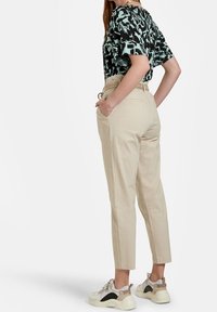 Pantaloni di cotone beige con vita aderente e tasche laterali, abbinati a un top con motivo astratto nero e verde menta e sneakers chunky.