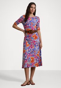 Vestito floreale con maniche corte, scollatura rotonda e vita aderente. I colori includono blu, arancione, rosa e viola, con un cinturino in evidenza.