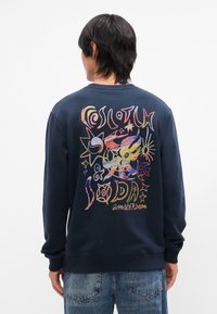 Sweatshirt bleu marine avec un design graphique coloré au dos, présentant des étoiles et des formes abstraites, tissu texturé, col rond et poignets côtelés.