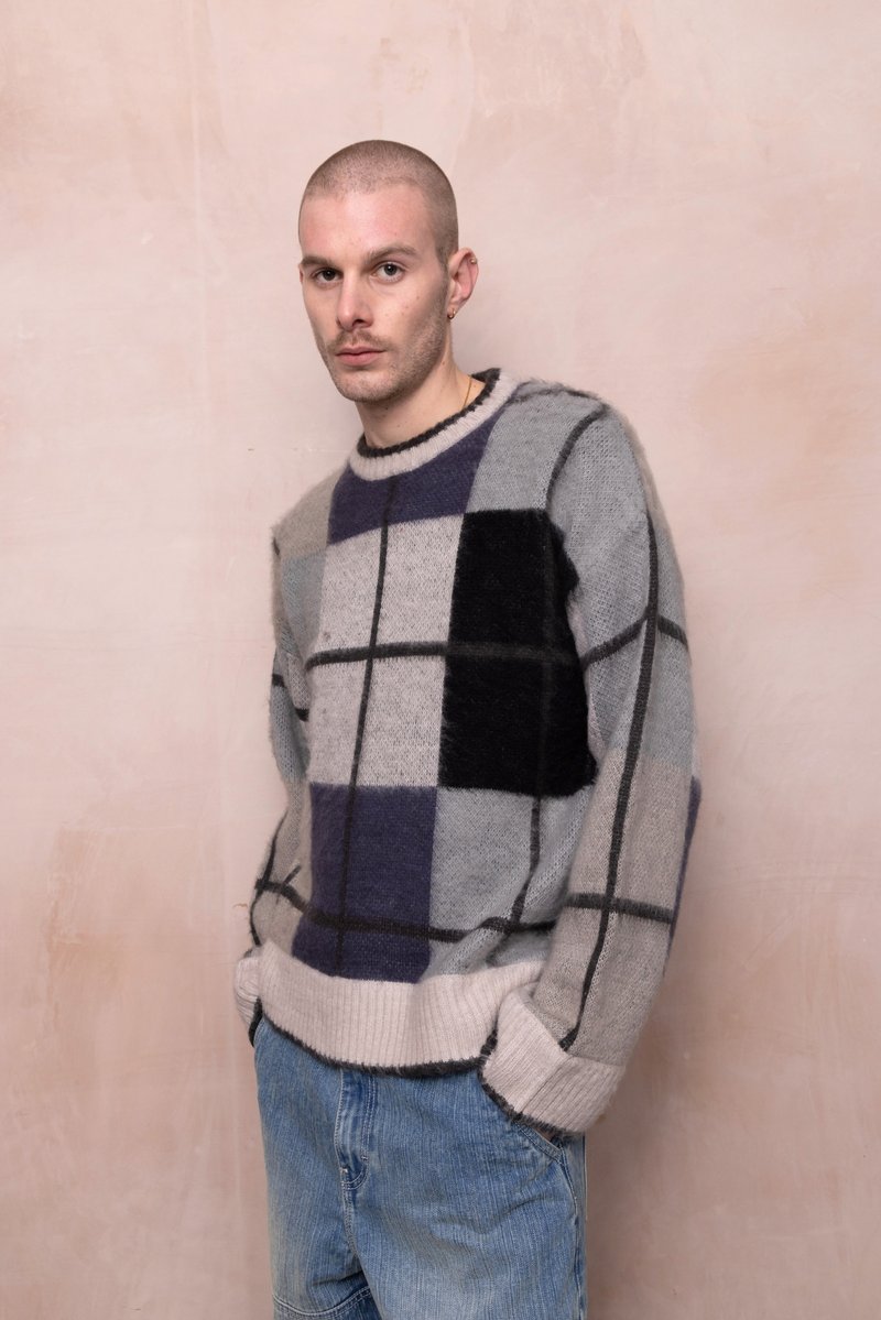 Pulover cu un model gri și negru, cu croială lejeră, cu decolteu rotund și margine cu nervuri, purtat peste pantaloni scurți din denim.