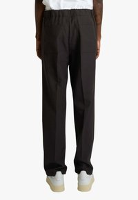 Pantaloni neri, ampi, in tessuto strutturato, con elastico in vita e due tasche sul retro, abbinati a sneakers bianche.