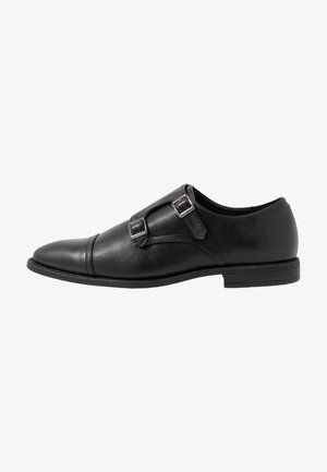 Chaussure habillée en cuir noir avec un design épuré, dotée de deux boucles en métal, d'un bout pointu et d'une semelle contrastante.