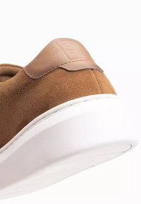 Baskets en daim marron avec une semelle en caoutchouc blanche. Présente une accent en cuir tan au niveau du talon, une texture lisse et un design minimaliste.