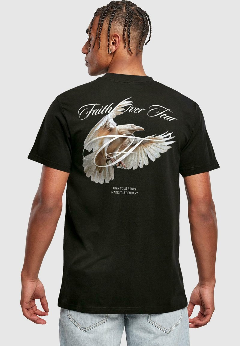 T-shirt en coton noir avec un graphique d'un oiseau aux ailes déployées, le texte "La Foi sur la Peur", et d'autres phrases motivationnelles en dessous.