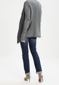 Šedý pletený svetr s dlouhými rukávy, volného střihu, v kombinaci s tmavými džínami s manžetami u kotníků a světle šedými botami na podpatku.