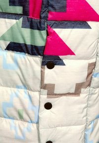 Tissu de veste matelassée colorée présentant des motifs géométriques en rose, vert, bleu et brun avec des boutons noirs le long de la fermeture.