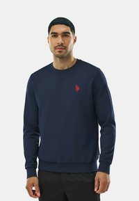 Felpa blu navy in tessuto dalla texture liscia, con logo rosso sul petto, scollo a girocollo e polsini e orlo a coste.