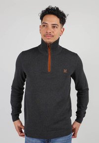 Sweat à fermeture éclair gris foncé avec un col haut et un accent de fermeture éclair orange. Présente une texture côtelée et une broderie de logo sur la poitrine.