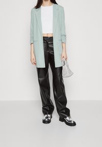 Jasnoniebieska marynarka, biała crop top, czarne spodnie z ekoskóry i srebrne buty na platformie. Teksturowany materiał w luźnym kroju. Mała biała torba.