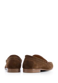 Mocasines de ante marrón con un tacón bajo, punta redondeada y costuras en contraste. Interior de cuero suave. Diseño minimalista sin marcas visibles.