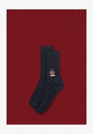 Mørkeblå ribstrikkede sokker med et farverigt broderet motiv af en rød bil med et juletræ på taget, sat mod en rød baggrund.